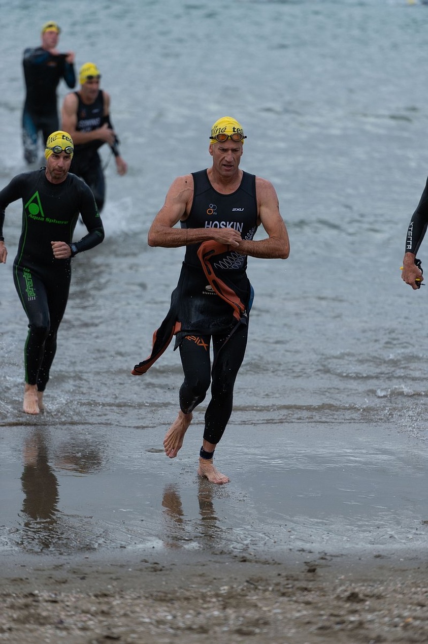 Triathlonatleter i våtdräkter och simmössor under ett lopp.